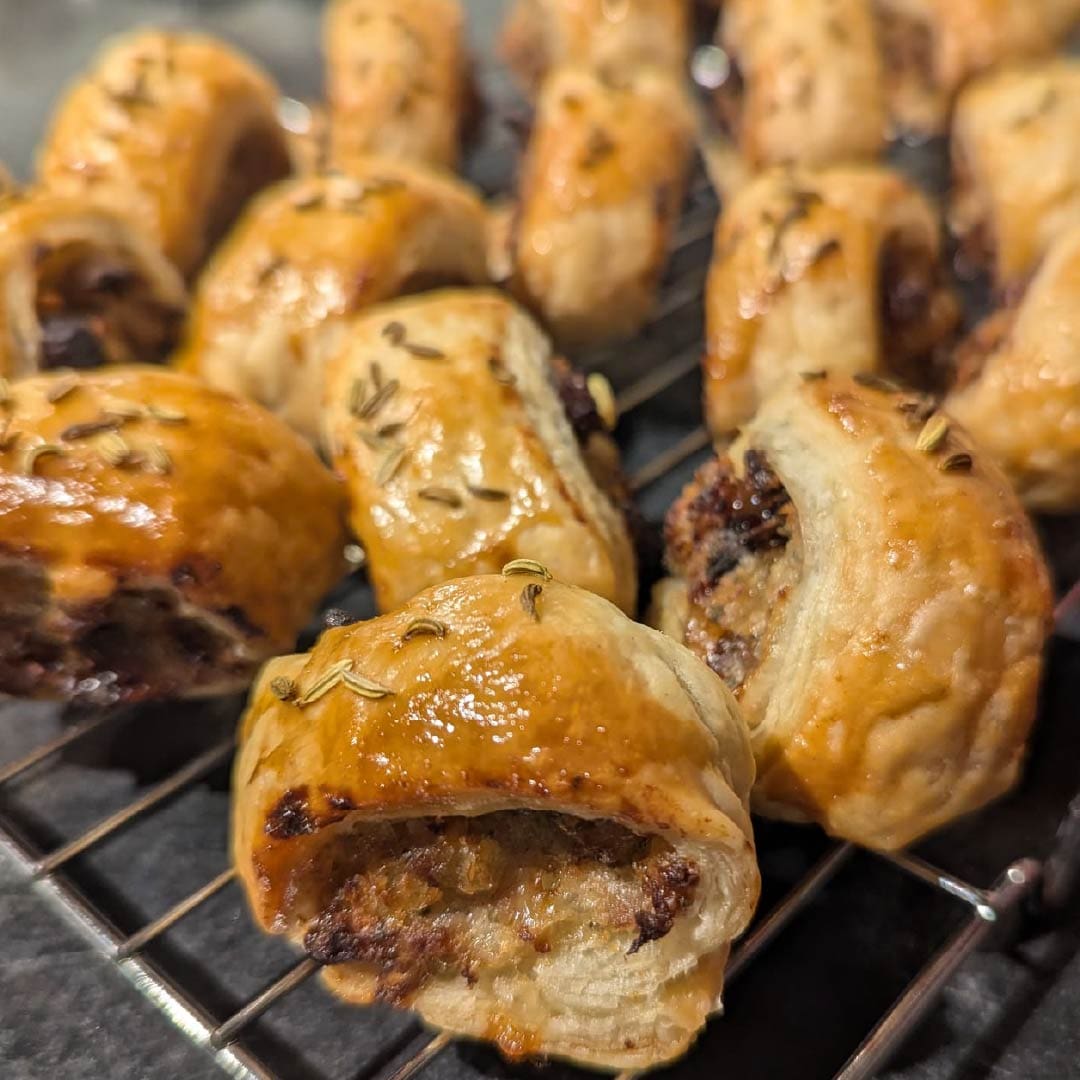 PMF Bacon Sausage Rolls, topped with fennel seeds and arranged on a cooling rack.
